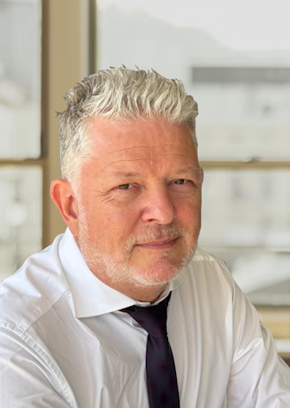 Lee facing the camera and smiling wearing a smart shirt and tie